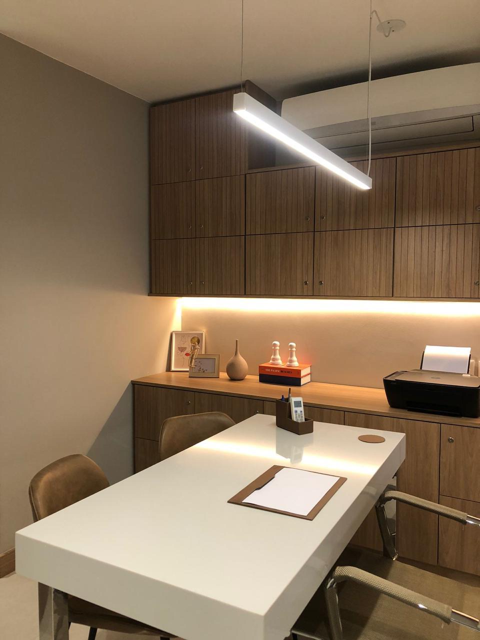 Consultório com mesa branca, marcenaria em madeira e iluminação suave